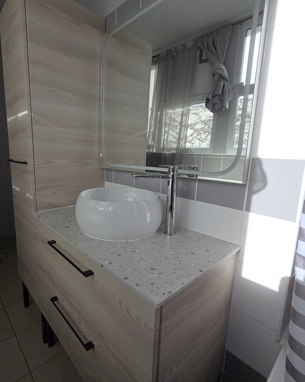 Meuble vasque en bois clair avec plan terrazzo, vasque ronde et miroir rétroéclairé dans une salle de bain rénovée à Montpellier